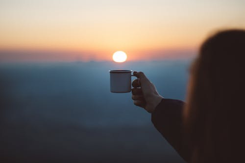 a woman raising a coffee cup while watching the sunset