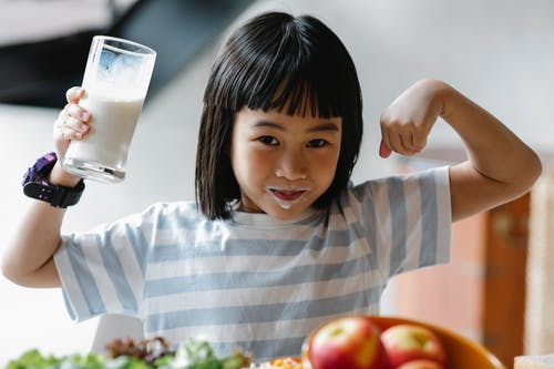 a child holding a glass of milk and showing his biceps