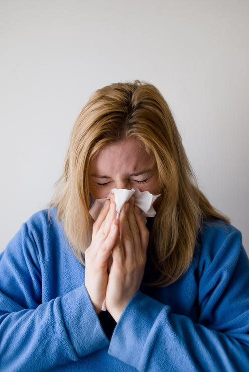 a woman in a blue pullover wiping her nose with a tissue