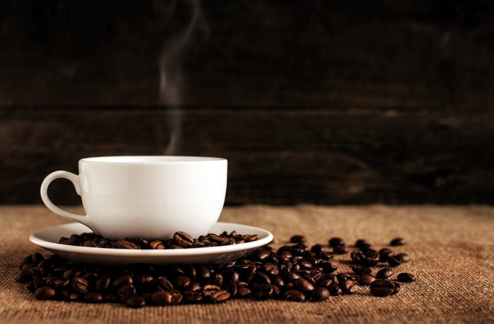 A hot cup of coffee surrounded by fresh coffee beans
