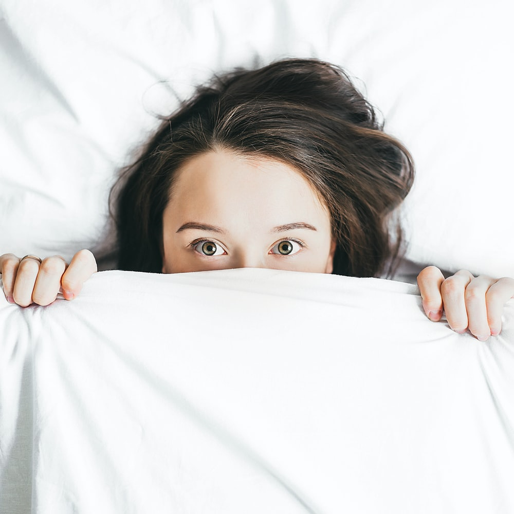 A girl lying in bed poking her head out of the bedsheet