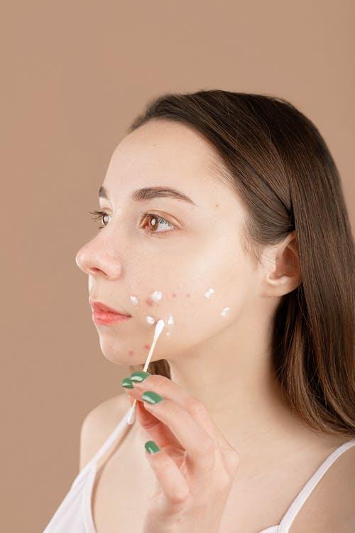 a woman putting ointment on her face using a cotton swab