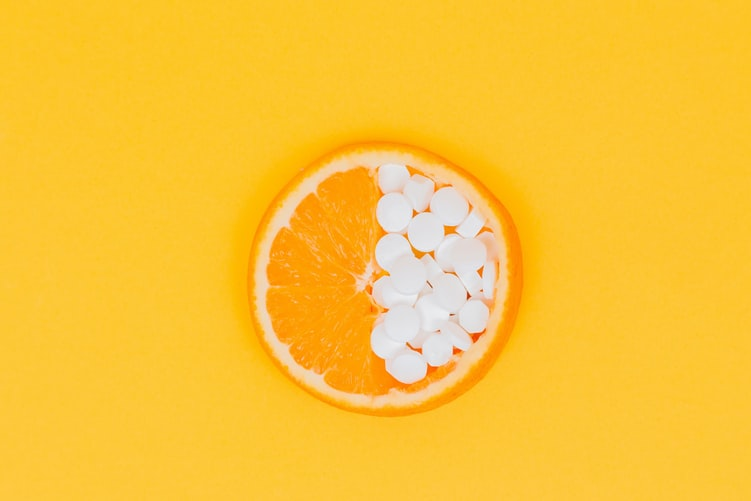 An orange slice showing half of it filled with Vitamin C supplement pills. 