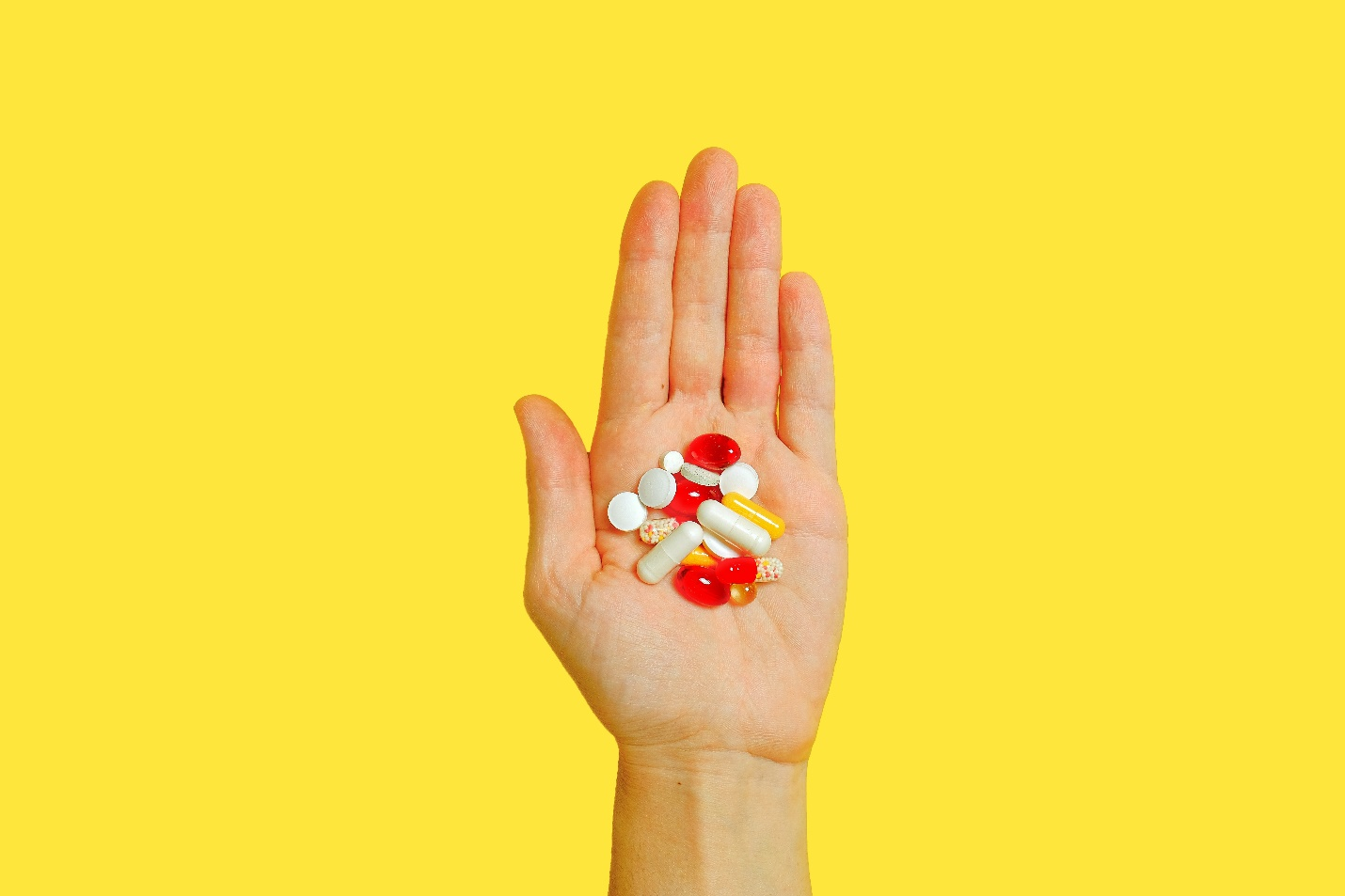 A hand holding out a bunch of tablets on a yellow backdrop