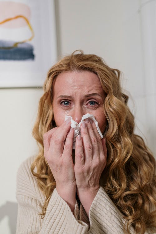 a woman with watery eyes blowing her nose