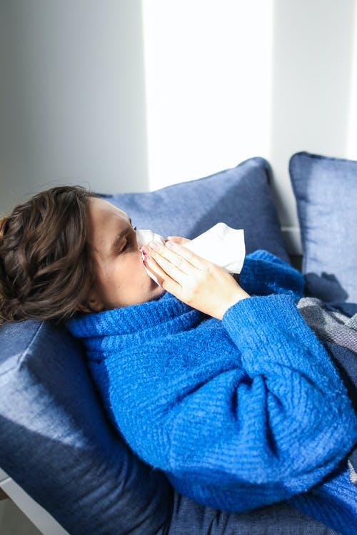 a woman in a blue sweater blowing her nose in a tissue