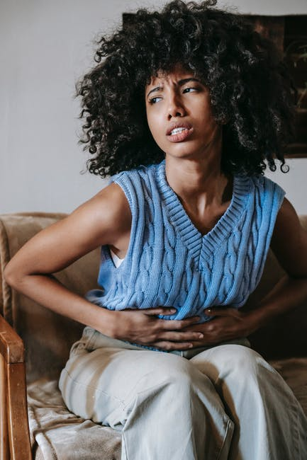  A woman with stomach pain sits in discomfort while holding her belly.