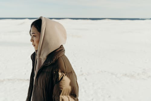 a woman in a brown hoody and puffer jacket standing on snow